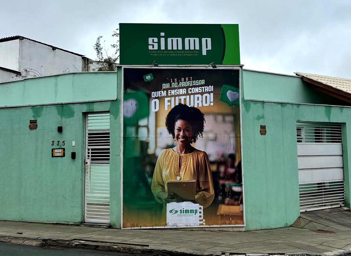 Fachada da sede do SIMMP em Vitória da Conquista, com a placa do sindicato e o cartaz do Dia do Professor